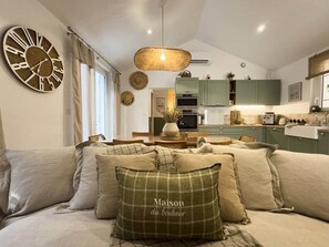 Ein gemütliches Wohnzimmer mit einer Couch, einer dekorativen Uhr und einer Küche im Hintergrund.