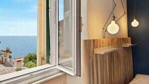 Une chambre dotée d’une grande fenêtre donnant sur la mer, d’une tête de lit en bois et de deux lampes suspendues.