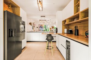 Eine moderne Küche mit einem Edelstahl-Kühlschrank, Holzregalen und einer zentralen Kochinsel mit einem schwarzen Stuhl.