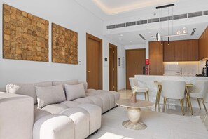 Ein modernes Wohnzimmer mit einem beigefarbenen Sofa, einem runden Couchtisch und einer Küchenzeile mit Holzschränken und einer Marmorarbeitsplatte.