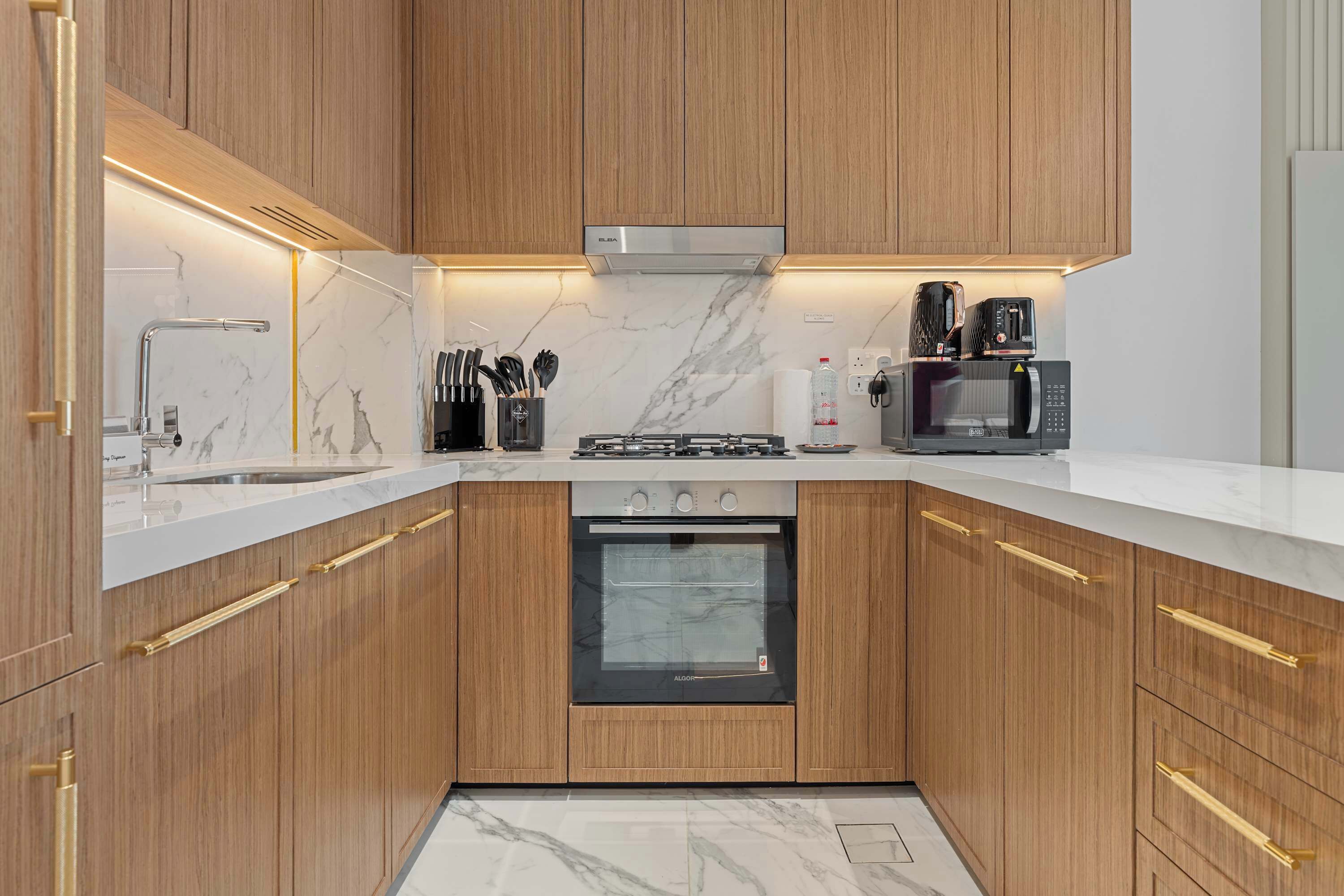 Une cuisine moderne avec des meubles en bois, une hotte en acier inoxydable, un four encastré et un four à micro-ondes.