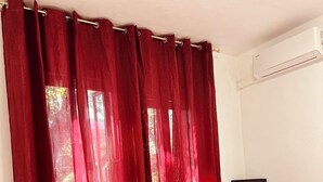 Ein Hotelzimmer mit einem Bett, roten Vorhängen, einem Schreibtisch mit einem Computer und einer Klimaanlage.