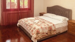 Ein Schlafzimmer mit Holzboden, einem Bett mit Blumenmuster und einem Nachttisch, sowie einem Fenster mit Vorhängen.
