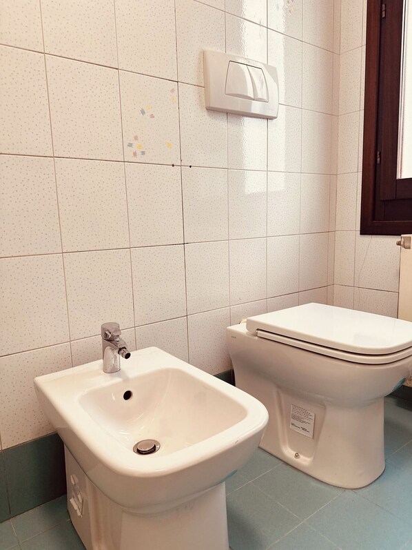 A bathroom with a bidet, a toilet, and a wall-mounted soap dispenser.