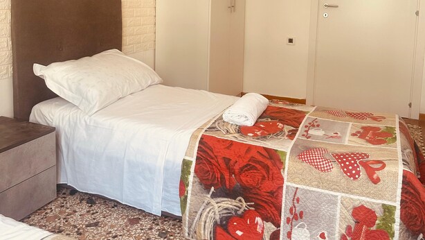 Um quarto com cama, mesa de cabeceira, guarda-roupa e uma porta.