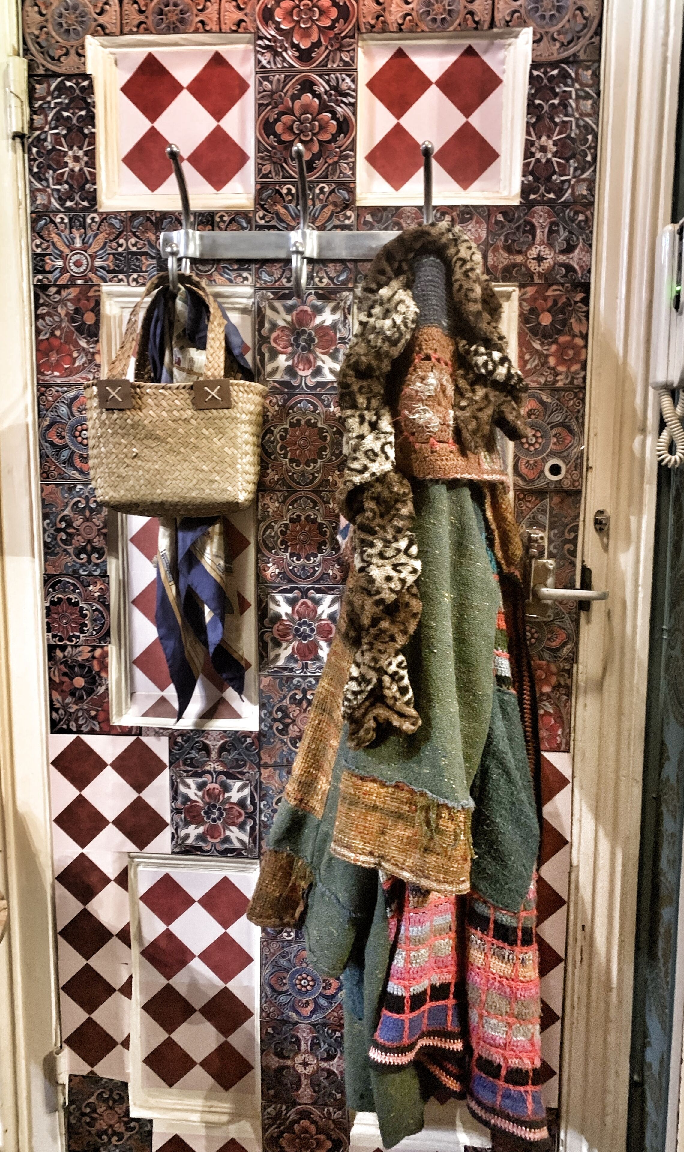 A door with a patterned tile design, a hanging woven bag, and a decorative garment.