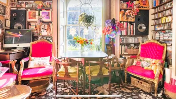 A cozy room with a large window, a dining table, two chairs, a television, and a bookshelf filled with books and decorative items. - Boutique Bijoux Garden Flat in Vibrant Oval (London)
