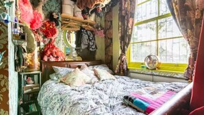 A room with a bed, a window with curtains, a fan, and various items on shelves and the bed. - Boutique Bijoux Garden Flat in Vibrant Oval (London)