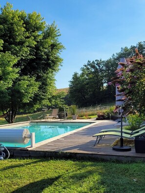 Ein Schwimmbecken mit Holzterrasse, umgeben von üppiger Vegetation und einer Erhebung im Hintergrund.