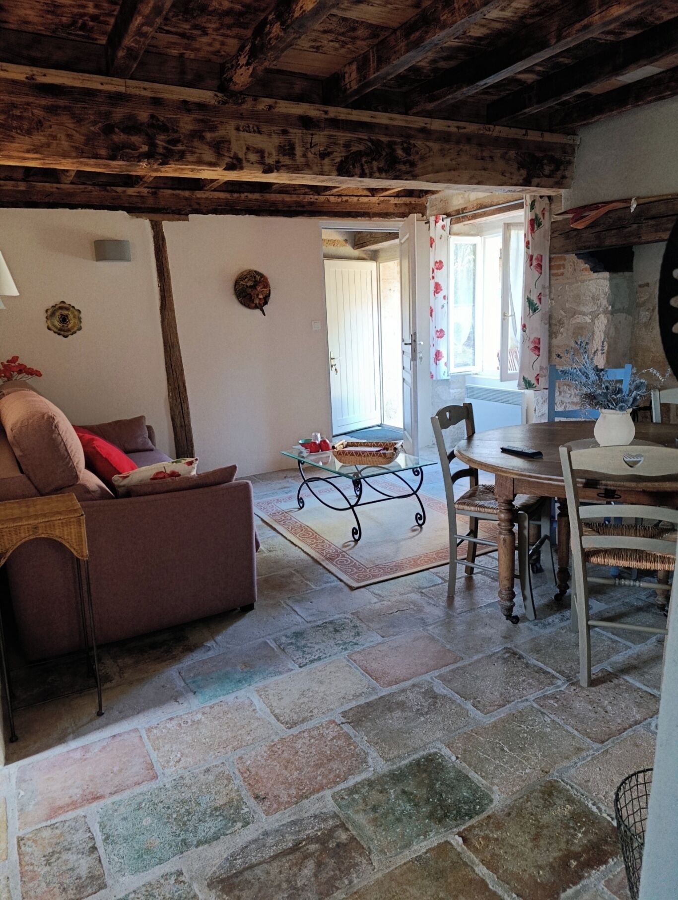 Una sala rústica con suelo de piedra, sofá de madera, mesa de centro de vidrio y mesa de comedor con sillas.