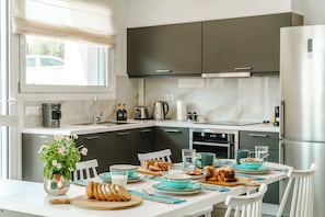 A modern kitchen with dark cabinets, a white countertop, and a dining table set for breakfast. - Estrella Luxury Villa | Refined Private Pool Living in Sivota, Greece (Sivota)