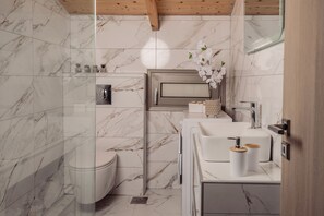 Un baño moderno con baldosas de mármol, inodoro, lavabo con espejo y zona de ducha.