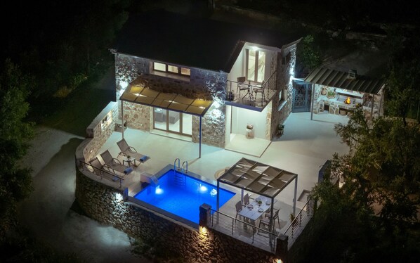 Una casa moderna con piscina, mobiliario exterior y fachada de piedra.