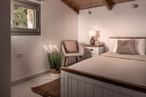 Un dormitorio con cama, una silla, una mesita de noche con lámpara y ventana con vistas a zonas verdes.