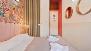 A hotel room with a bed, a wall with a decorative panel, a door, and a mirror.