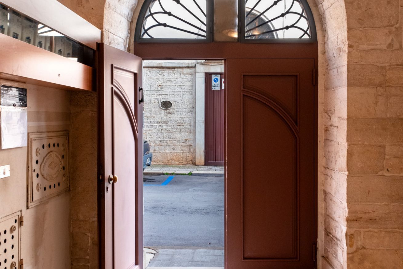 Une porte marron entrouverte donnant sur une rue bordée d’un mur de briques et marquée d’une ligne bleue au sol.