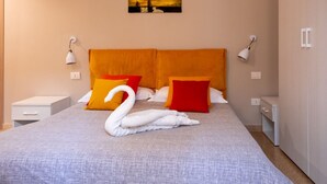 Una cama con una toalla con forma de cisne, dos almohadas naranjas y un cuadro de la ciudad en la pared.
