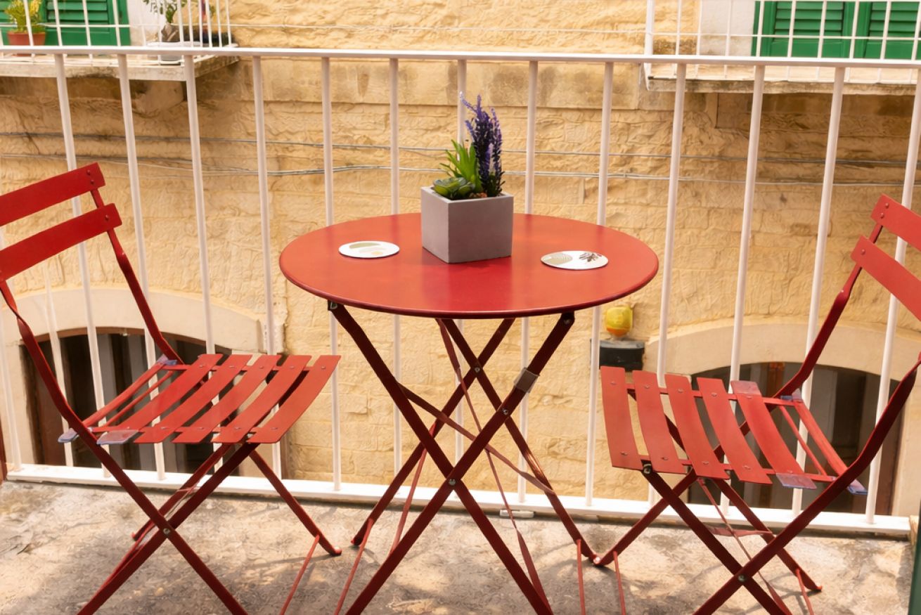 A balcony with a round table and two red chairs, a potted plant, and a white railing.