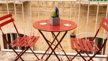 A balcony with a round table and two red chairs, a potted plant, and a white railing.