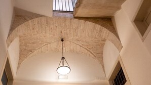 Techo abovedado con una lámpara colgante, una ventana con rejas y un muro de ladrillo.