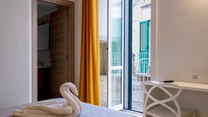 Habitación de hotel con cama, escritorio, silla, ventana con vista al exterior y puerta que da a otra habitación.