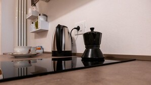 Una cocina con cafetera, hervidor y una taza sobre la encimera.