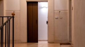 Un pasillo con una puerta de madera, una barandilla de metal y un interruptor de luz en la pared.