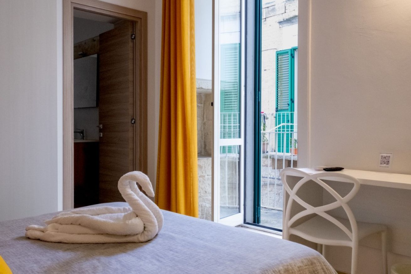 Une chambre d’hôtel comprenant un lit, un bureau, une chaise, une fenêtre donnant sur l’extérieur et une porte menant à une autre pièce.
