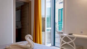 Habitación de hotel con cama, escritorio, silla, ventana con vista al exterior y puerta que da a otra habitación.