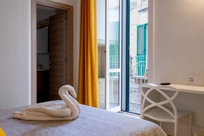 Ein Hotelzimmer mit einem Bett, einem Schreibtisch, einem Stuhl, einem Fenster mit Blick nach draußen und einer Tür zu einem anderen Raum.