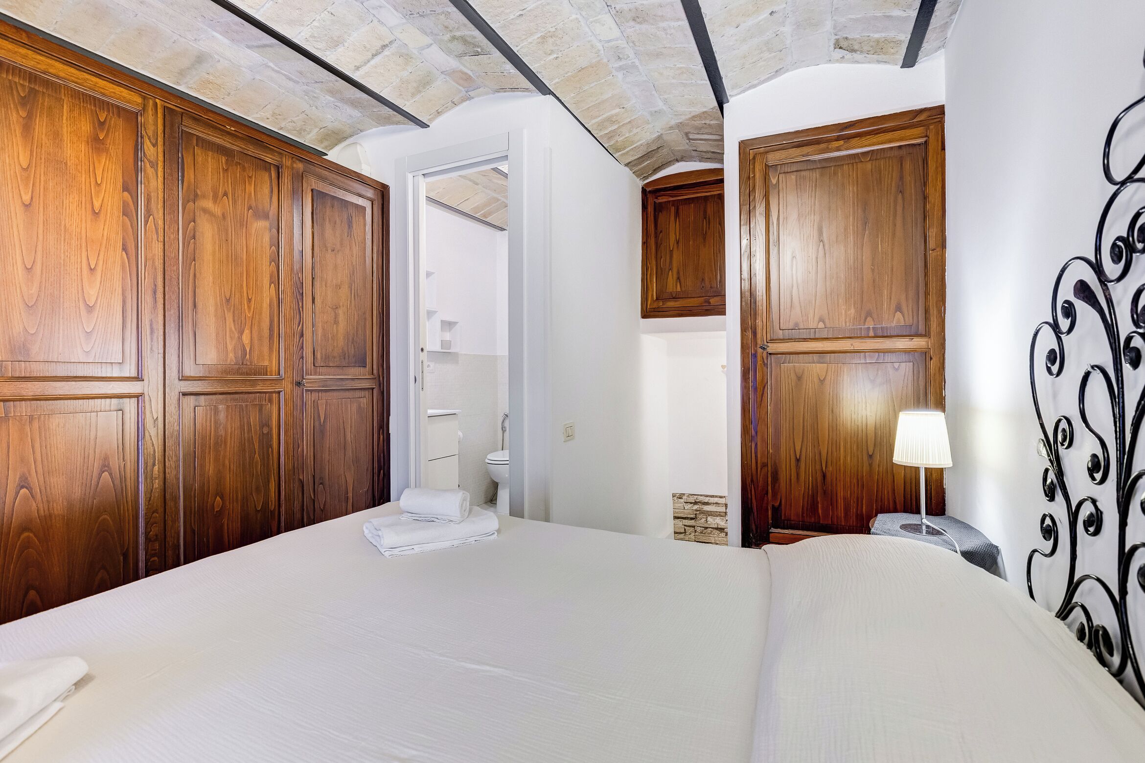 A hotel room with a large bed, wooden wardrobe, and a bathroom visible through an open door.