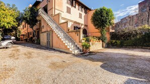 A two-story building with a staircase leading to the entrance, surrounded by gravel and potted plants. - Charming Apt with Garden and Park (Rome)