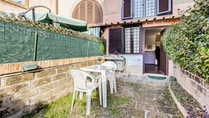 A courtyard with a stone pathway, a white table and chairs, and a green fence. - Charming Apt with Garden and Park (Rome)