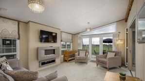 Un salón amplio con televisión de pantalla plana, asientos cómodos, una mesa de centro de madera y un ventanal con vistas al exterior.