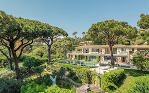 A modern villa with a swimming pool, surrounded by lush greenery and tall trees. - Le Faune, exceptional villa with tennis court (Ramatuelle)