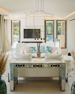 A modern living room with a central coffee table, a sofa set, and a television mounted on the wall. - Le Faune, exceptional villa with tennis court (Ramatuelle)
