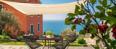 A patio with outdoor furniture, a view of the sea, and a building with a red facade.