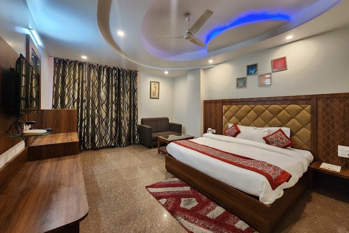 A hotel room with a bed, a desk, a sofa, a TV, and a ceiling fan.