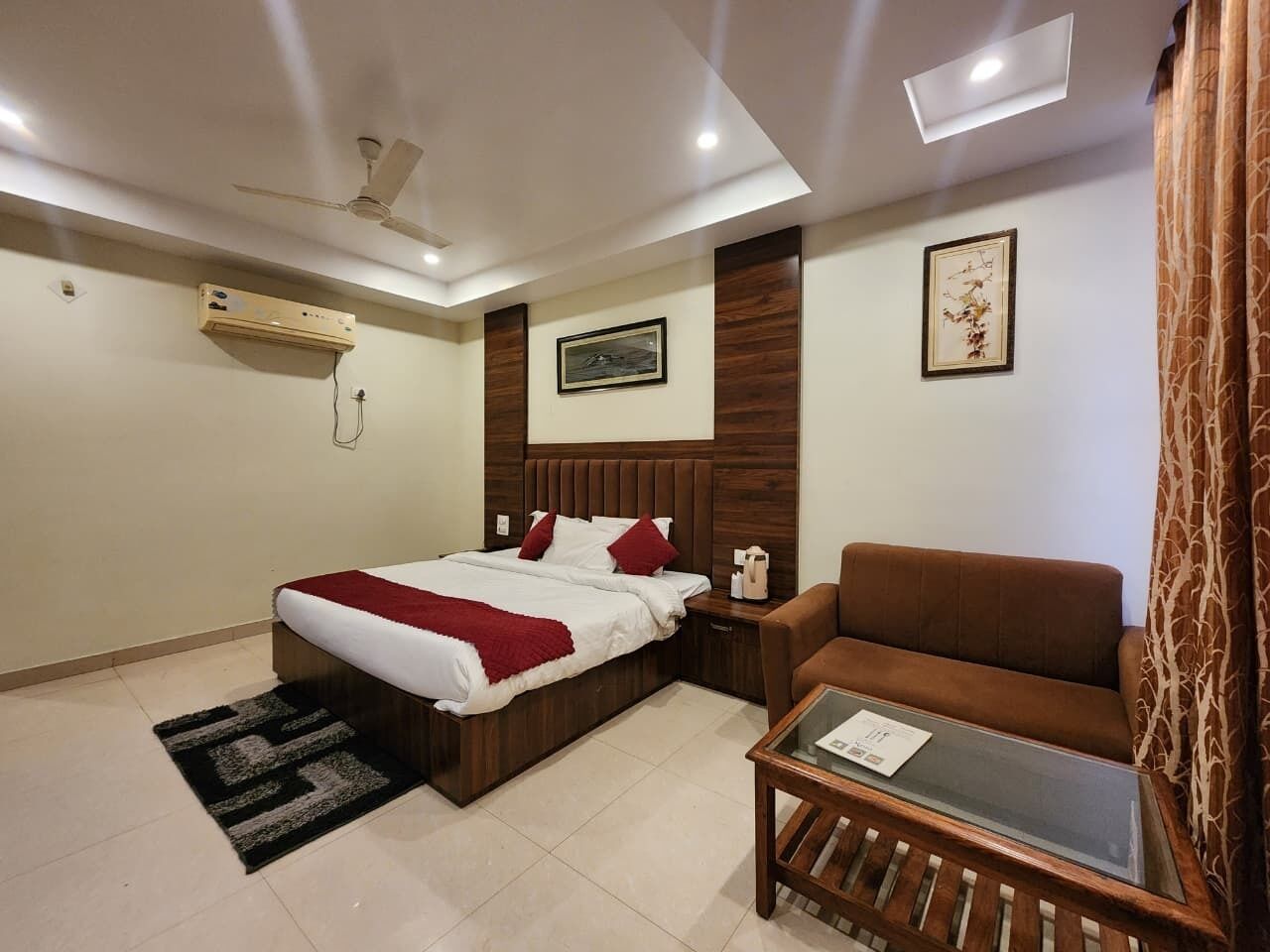 Una habitación de hotel con cama, sofá, una mesita, aire acondicionado, ventilador de techo y un cuadro en la pared.