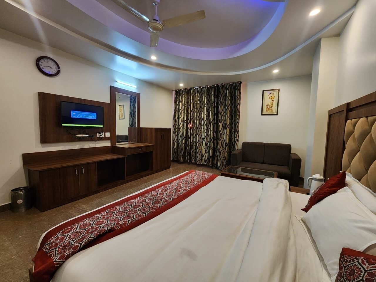 A hotel room with a bed, a desk, a television, a sofa, and a ceiling fan.