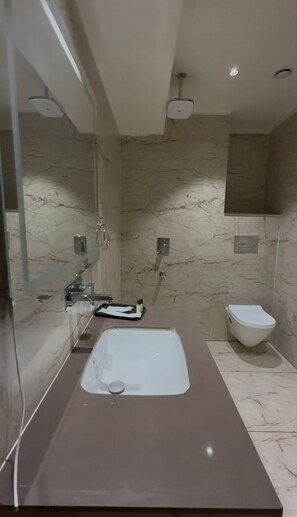 Een moderne badkamer met een marmeren wastafel, een douche met glazen wanden en een toilet.