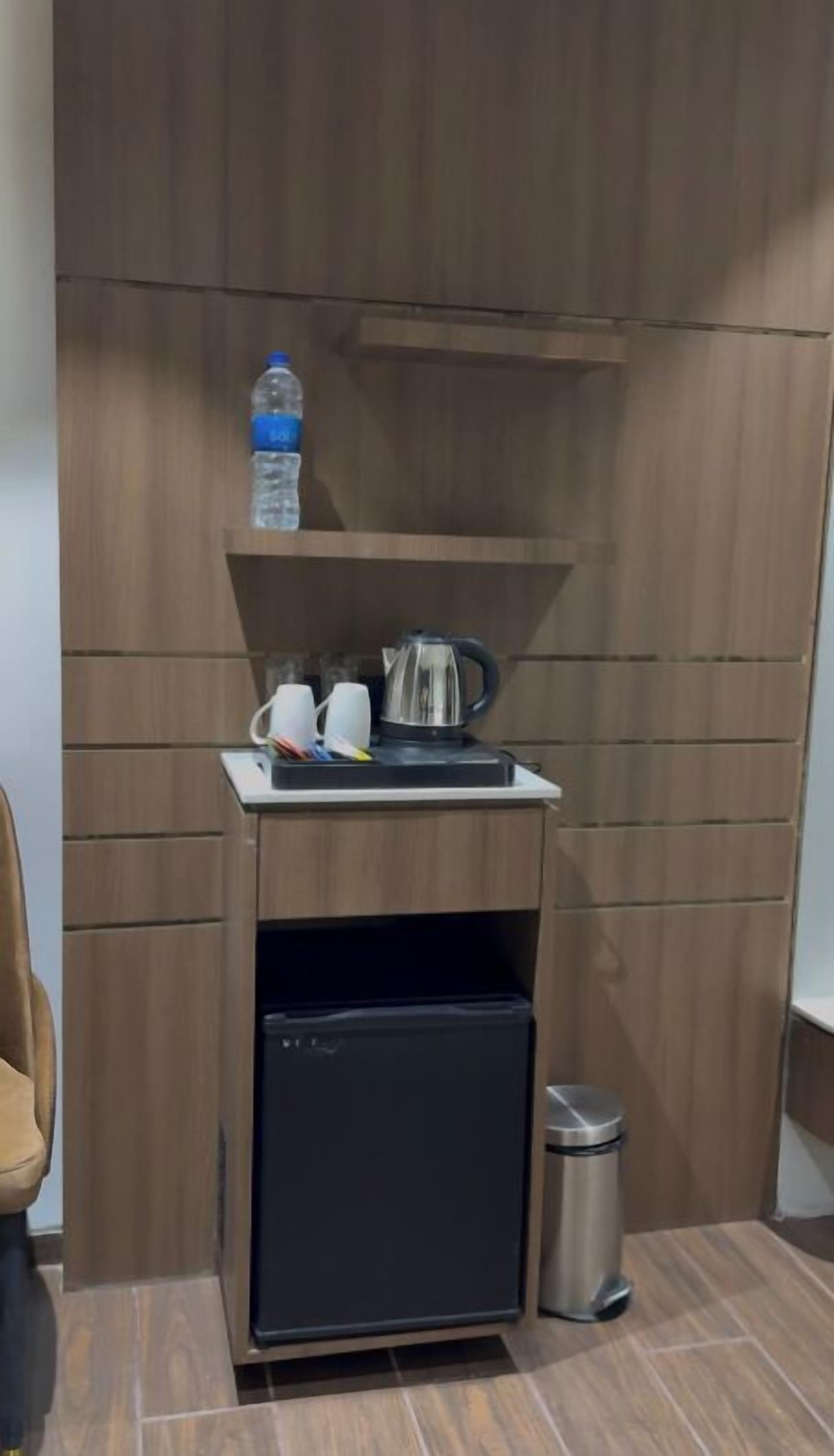 Una kitchenette compacta con un refrigerador empotrado, un lavamanos y una tetera sobre la encimera.