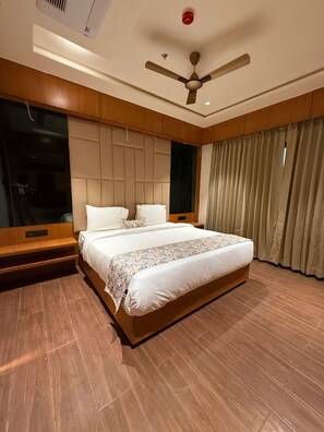 Een moderne hotelkamer met een groot bed, houten lambrisering, een plafondventilator en een raam met gordijnen.
