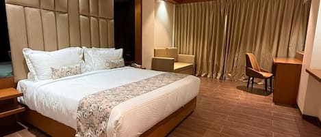 A modern hotel room with a large bed, a desk, a chair, and a ceiling fan.