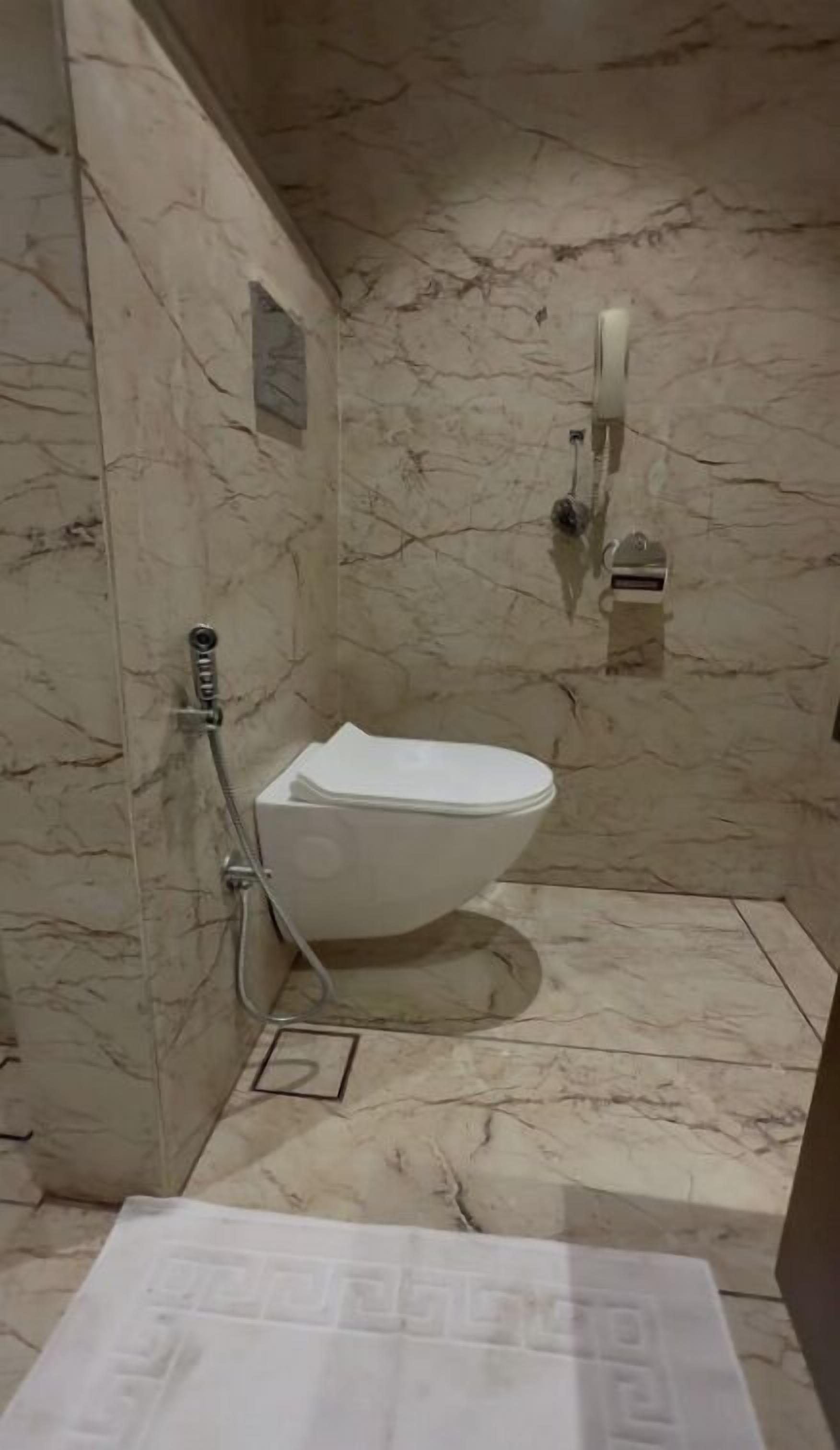 A bathroom with a toilet, a shower, and a marble floor.