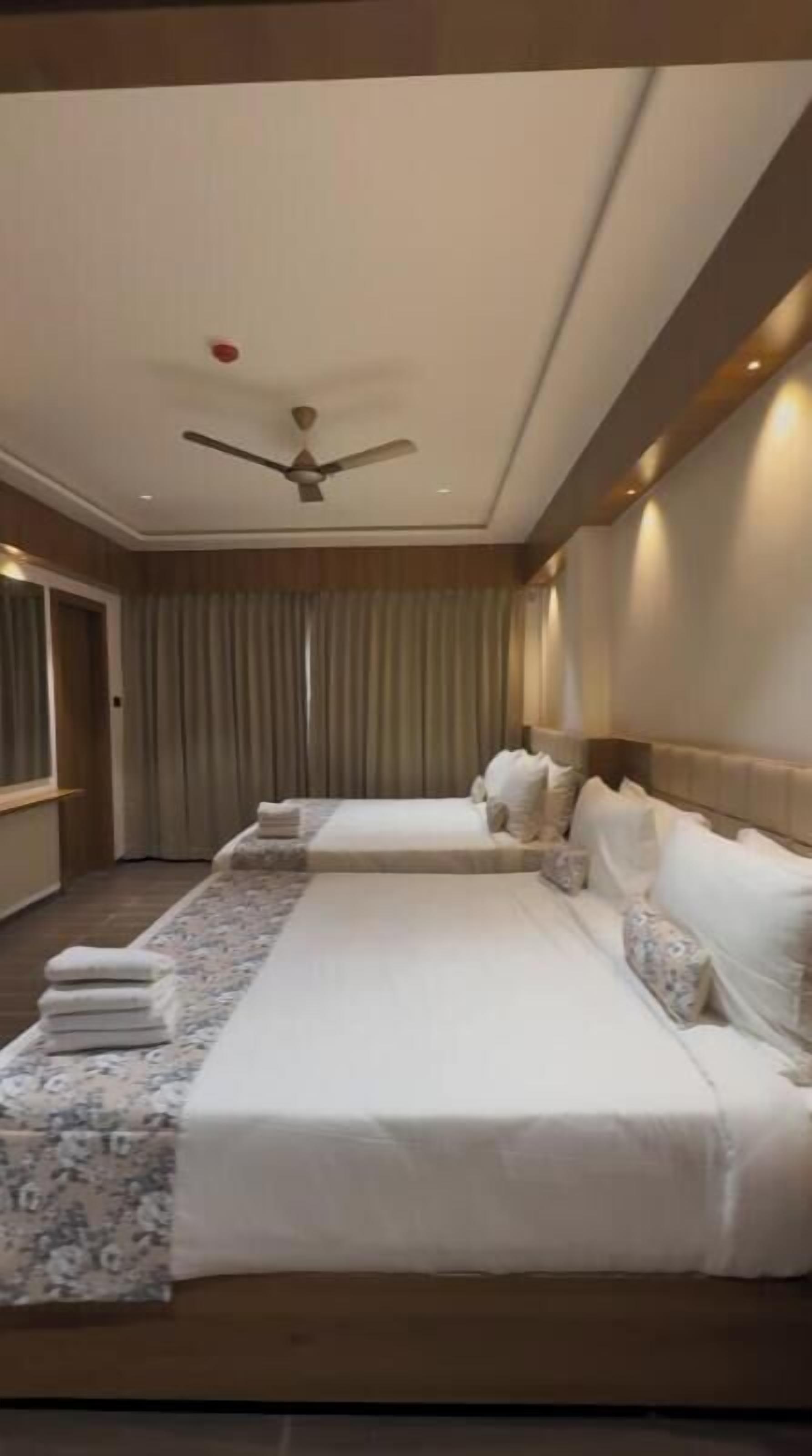 A hotel room with two beds, a ceiling fan, and a large window with curtains.