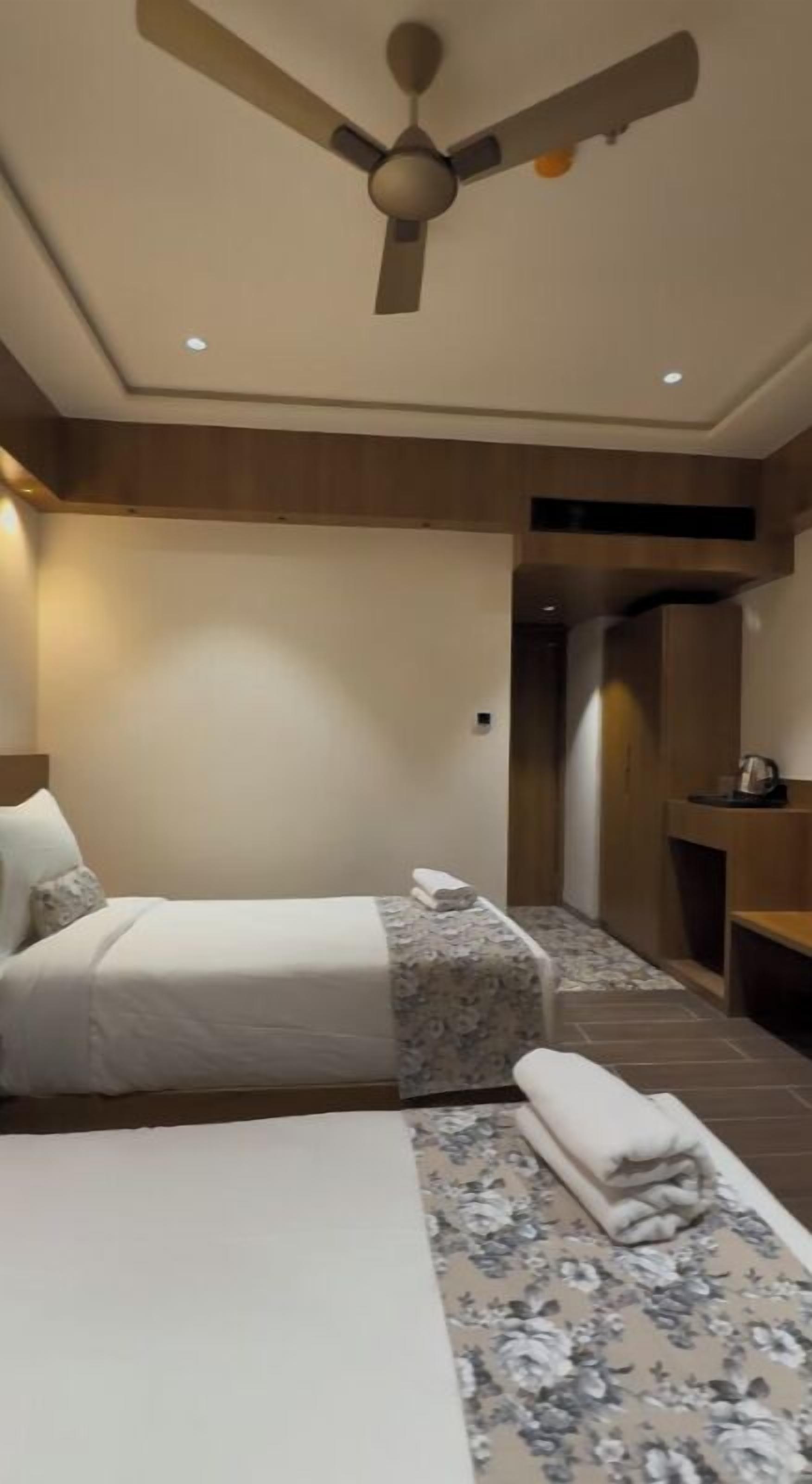 Ein Hotelzimmer mit zwei Betten, einem Deckenventilator und einer kleinen Sitzecke.