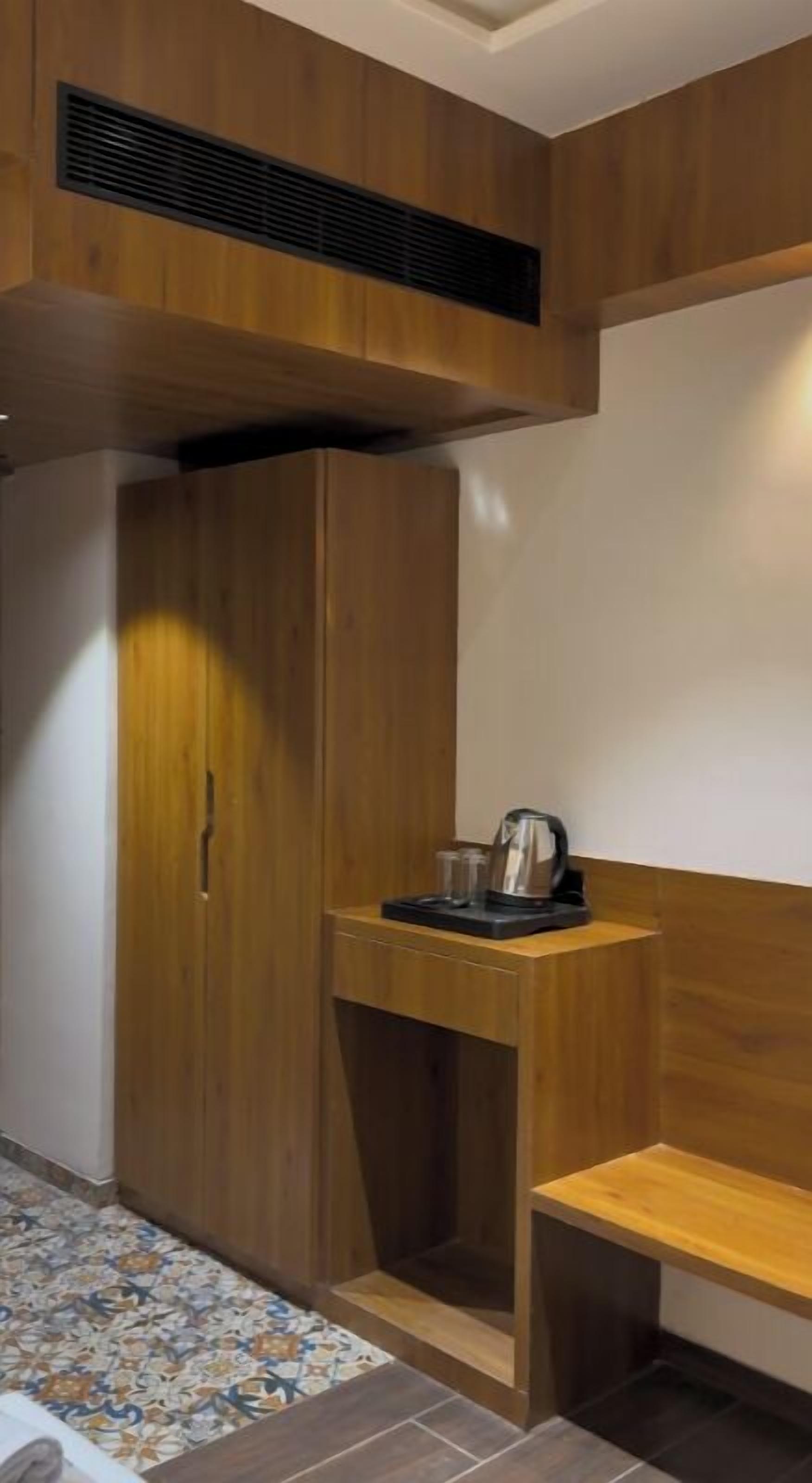 A compact room with a wooden wardrobe, a small table with a kettle, and a bench.