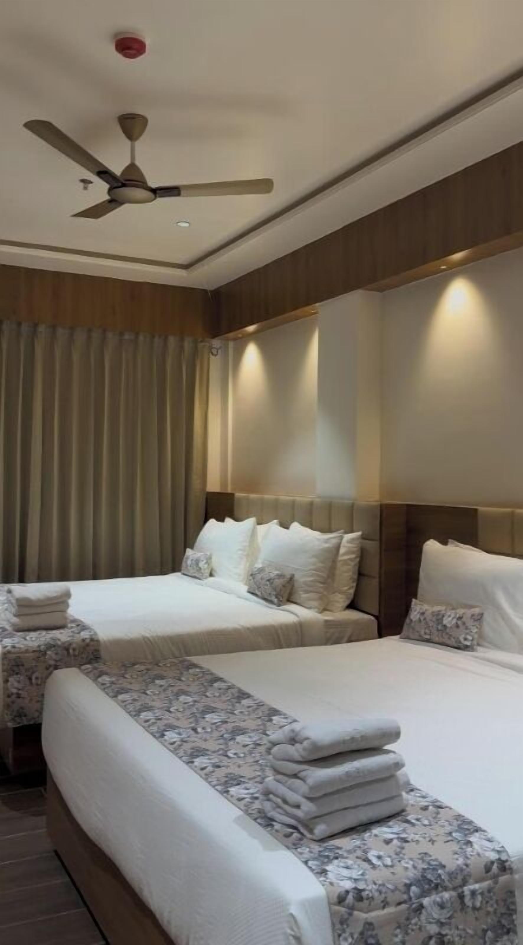 A hotel room with two beds, a ceiling fan, and a large window with curtains.