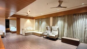 A spacious living room with a wooden ceiling, a sofa set, a coffee table, and a large window with curtains. - Hariganga S The Lake Attitude (Amravati)